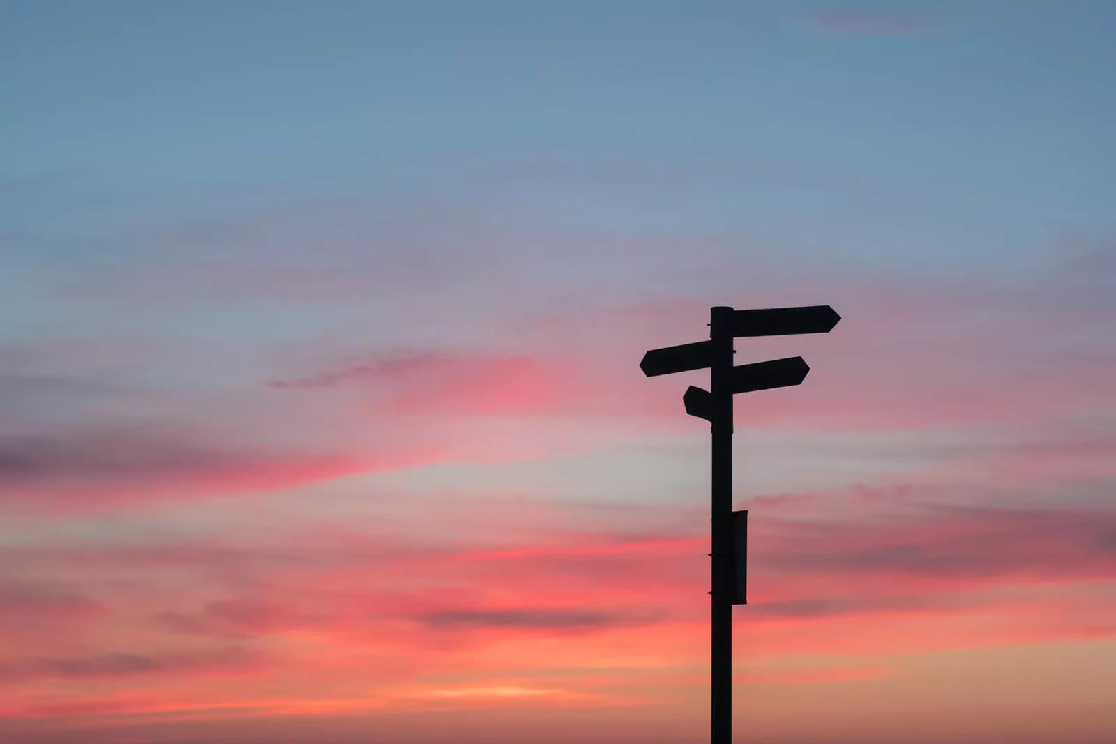 A signpost pointing several ways, silhouetted against a sunset sky